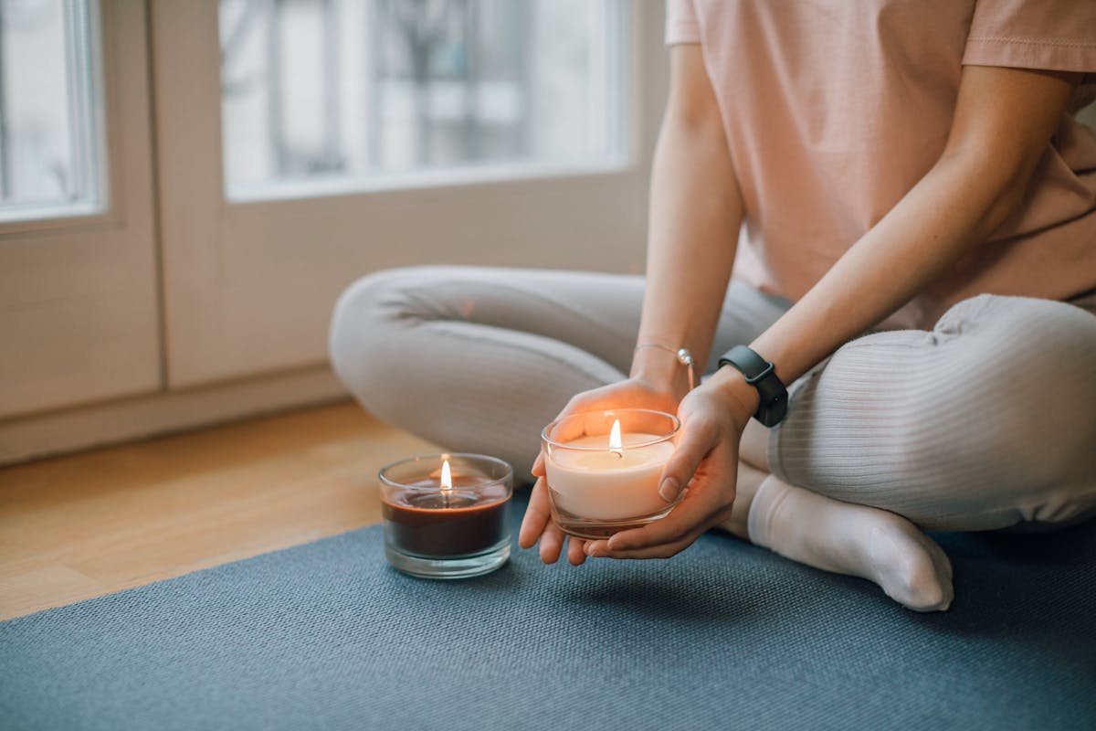 A person sitting cross-legged holding a lit candle in a candlelit meditation space