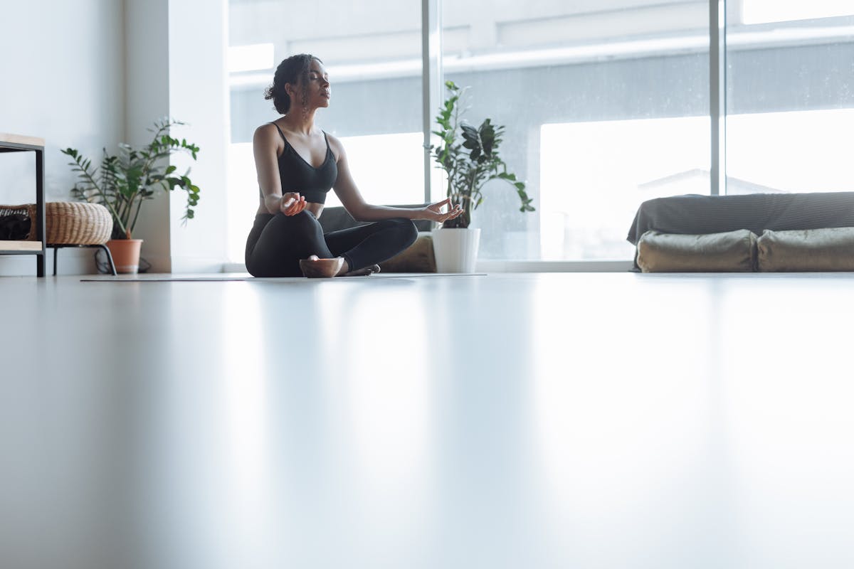 A woman meditating near a large window with soft natural light filling the room