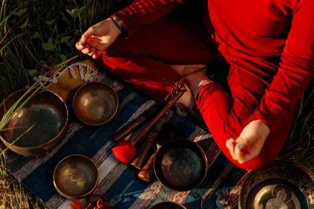 A person seated in outdoor meditation with a Tibetan singing bowl in a natural setting