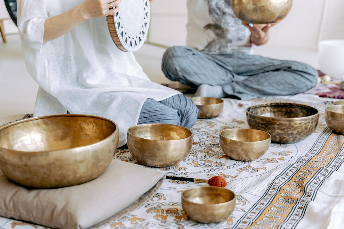 Two people seated in meditation alongside Tibetan singing bowls in a softly lit space